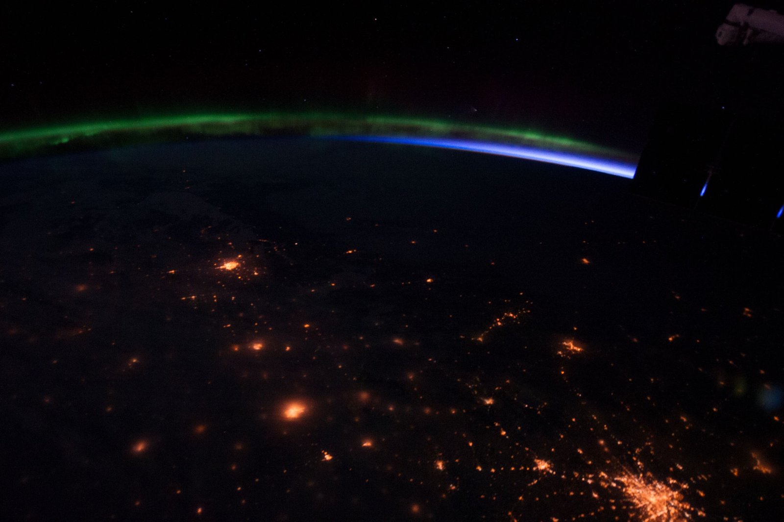 The northern lights and an orbital sunrise over city lights, photographed from the International Space Station
